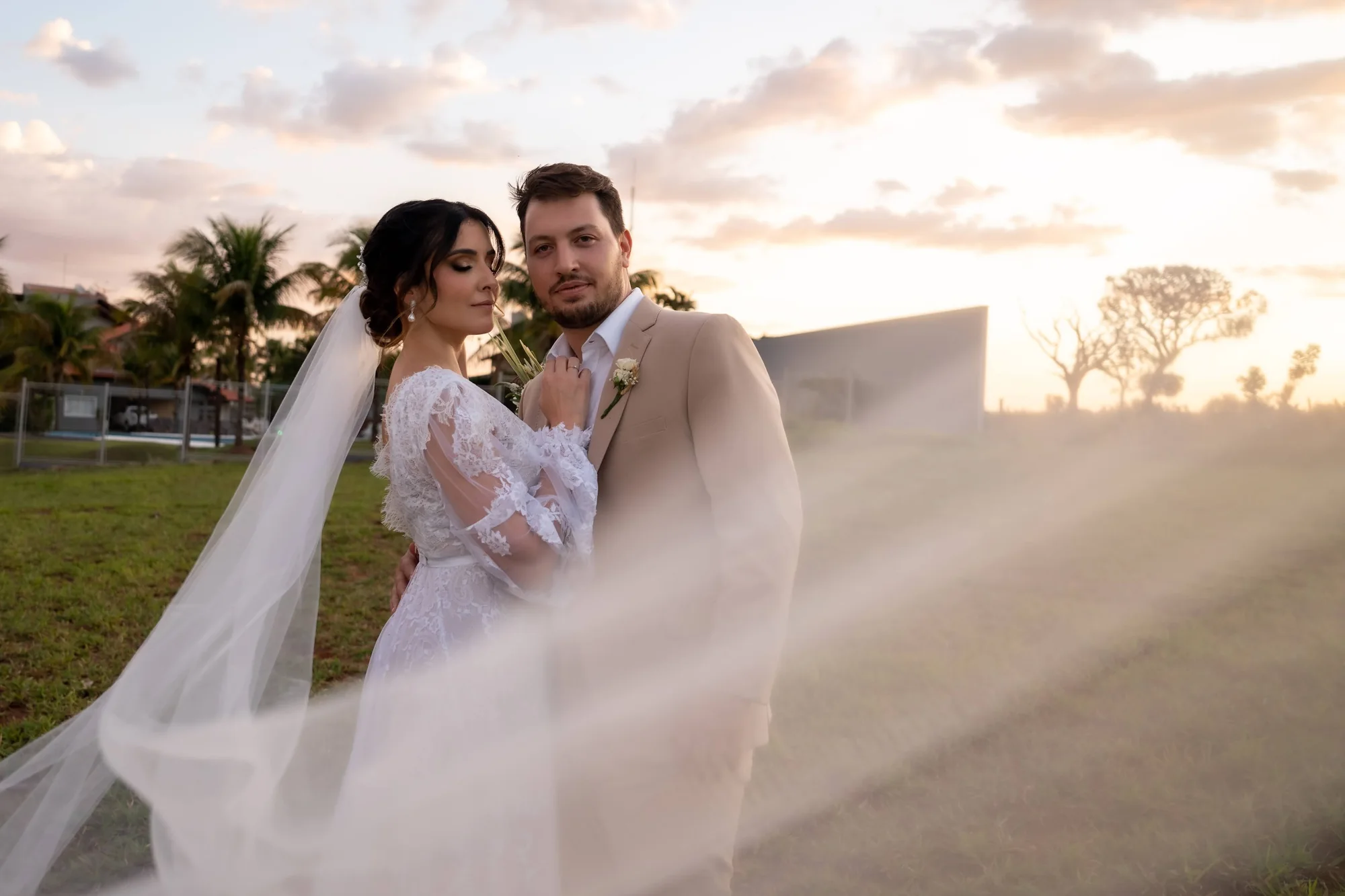 Noivos juntos, envolvidos pelo véu e pela luz do fim de tarde